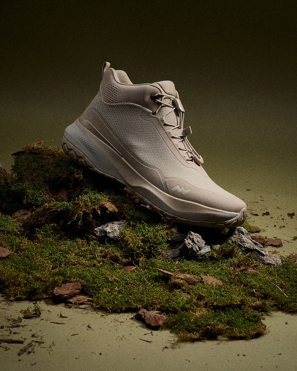 Muddy Vibe Zn-30 Desert Sand mid-top hiking shoe on moss and rocks side view on a soft dark green background.