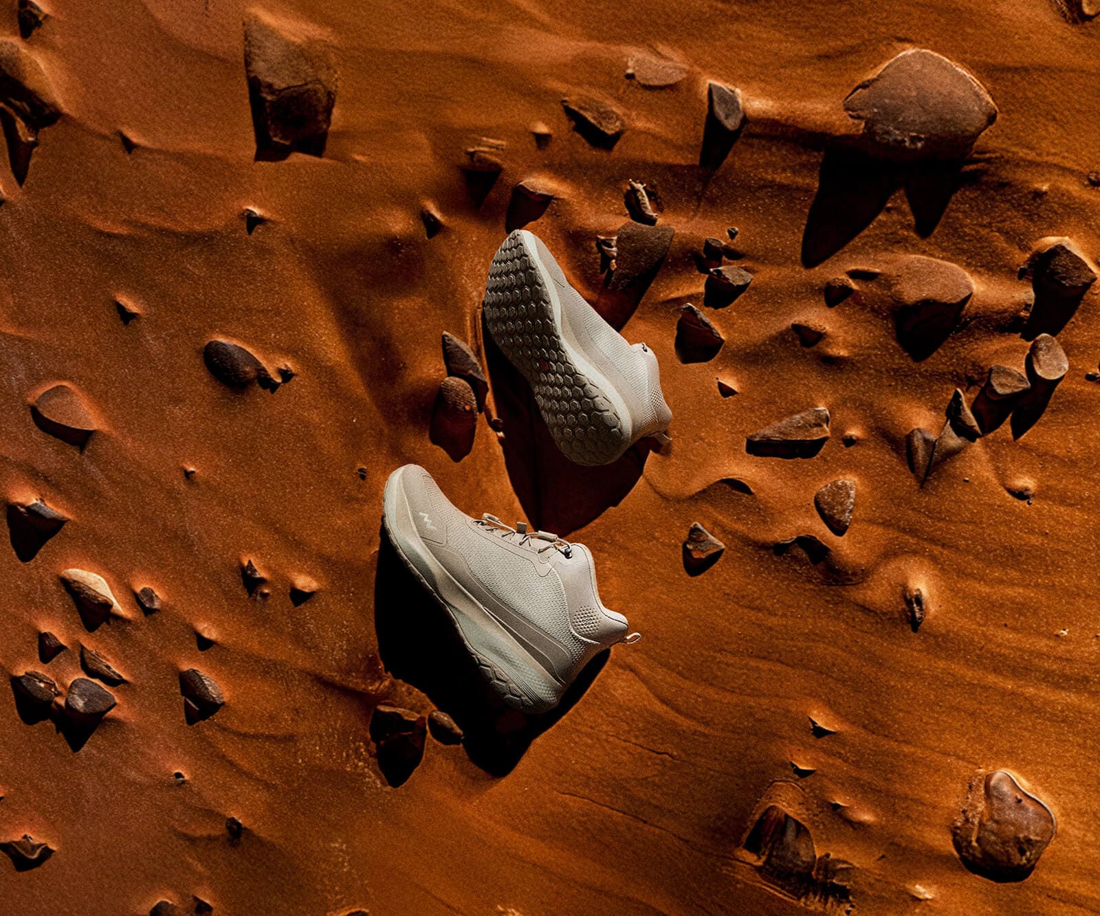 MUDDY VIBE Zn-30 Desert Sand mid-top hiking shoe with light beige and off-white accents on a reddish sandy surface with rocks.