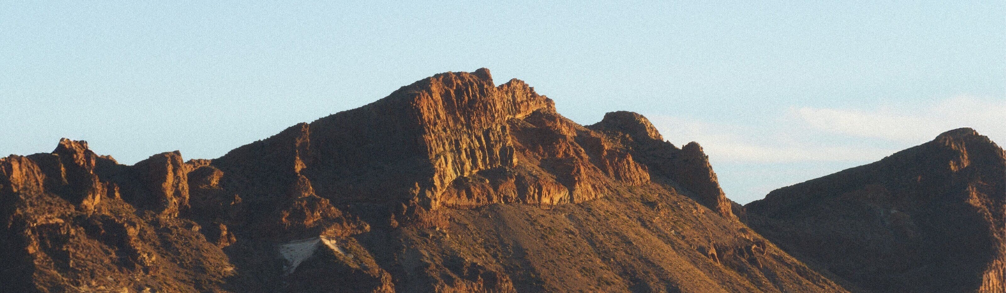 Image from MUDDY VIBE. A mountain range with rugged brown rocks under a clear sky.