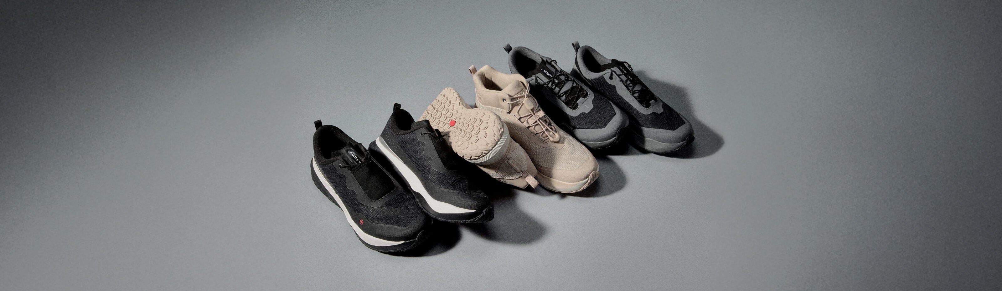 Three pairs of MUDDY VIBE shoes are randomly placed on a soft shadow background. The shoe styles and colors from left to right are S-16-ridge-snow, Zn-30-desert-sand and Si-14-tide-rock.