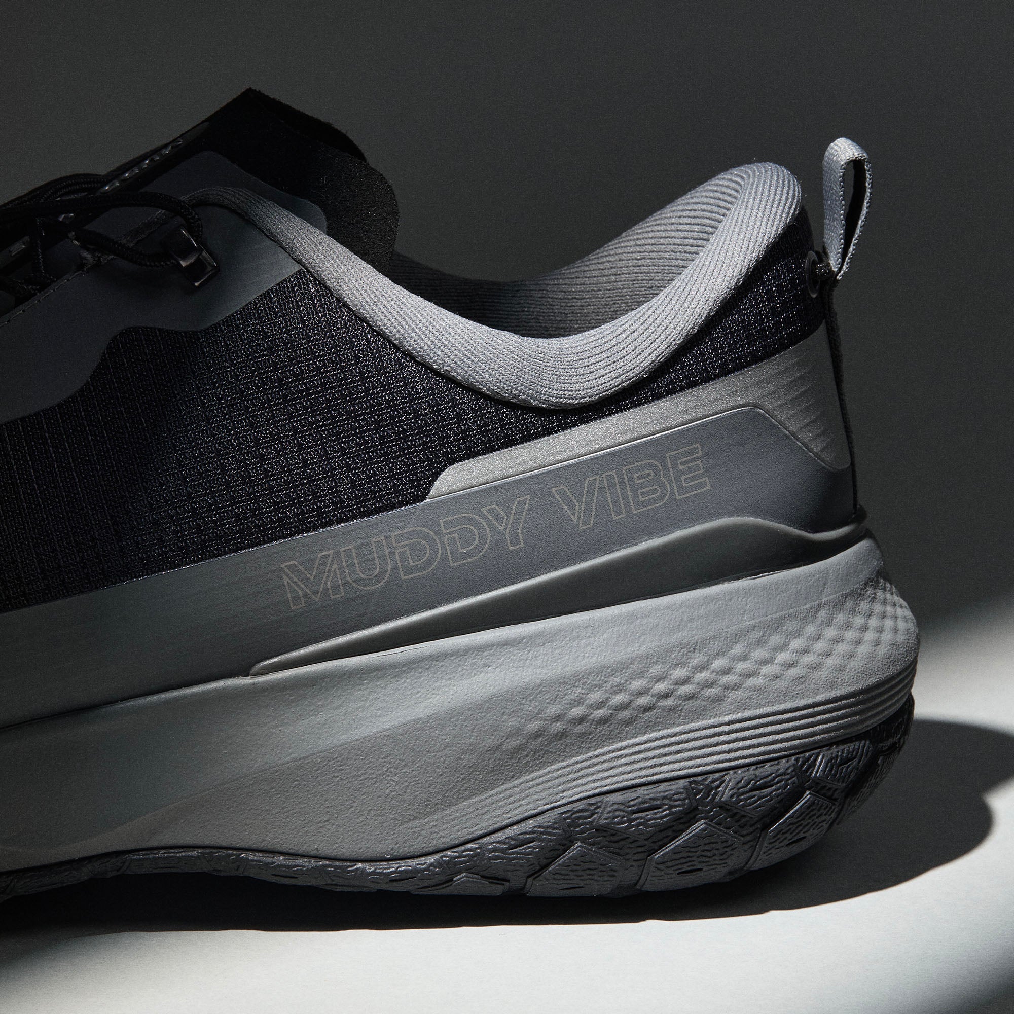 MUDDY VIBE Si-14 Tide Rock low-top hiking shoe with black and grey accents, heel logo view on a soft shadow background.