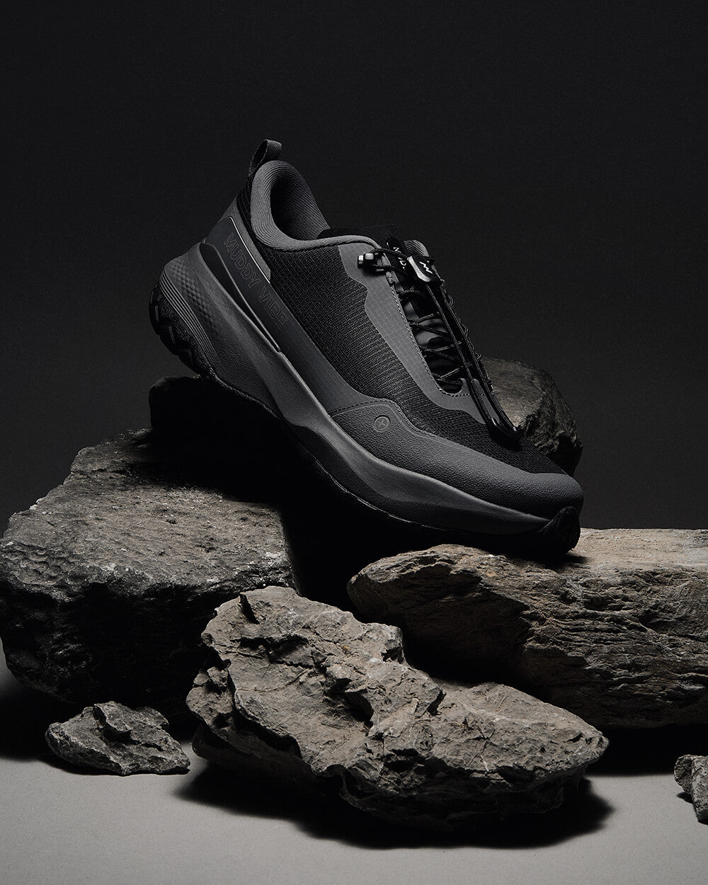 MUDDY VIBE Si-14 Tide Rock low-top hiking shoe on rocks, black background with soft lighting. 